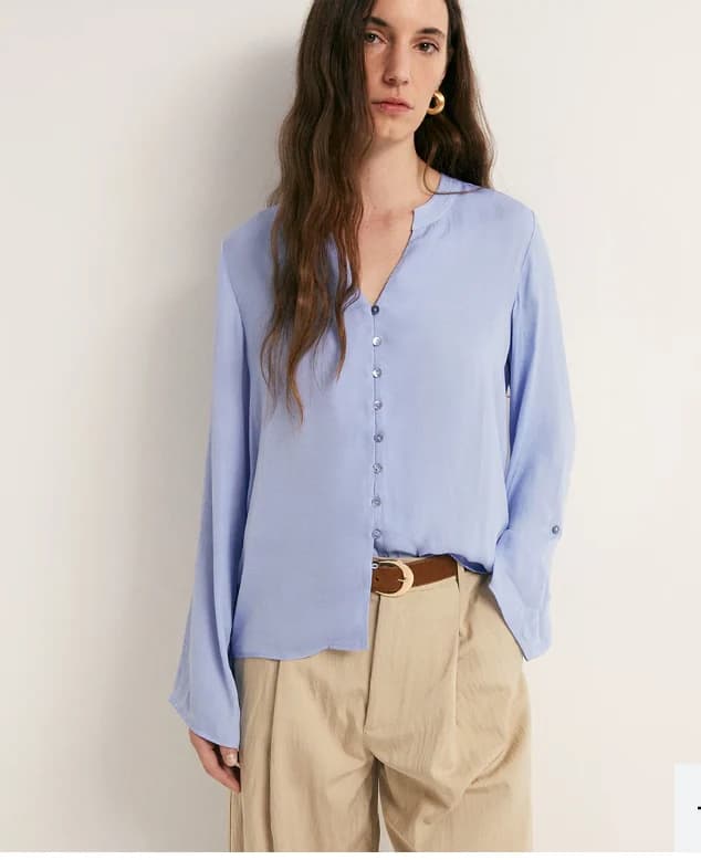 Soft blue woven blouse with fluid drape and minimal hardware.
